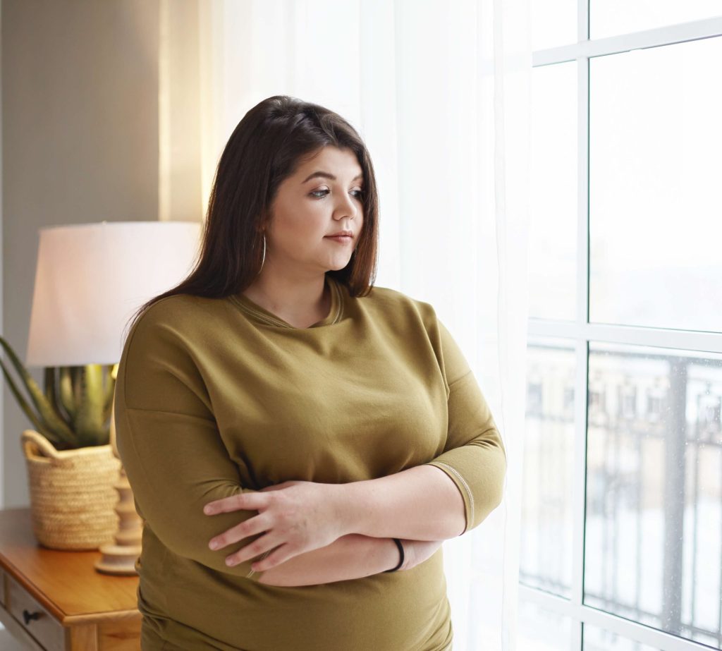 People Lifestyle Body Positivity Concept Beautiful Young Brunette Female With Extra Pounds Standing By Window Home Crossing Arms Her Chest Having Thoughtful Pensive Look Pondering E1763210073946 1024x923